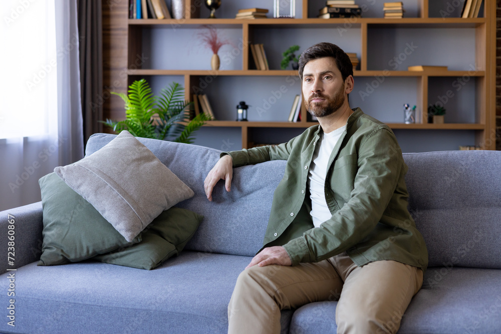 Man sitting on sofa at home, serious and thinking in casual shirt, mature guy in living room relaxing in day. Man sitting on sofa at home, serious and thinking in casual shirt, mature guy in living room relaxing in day.