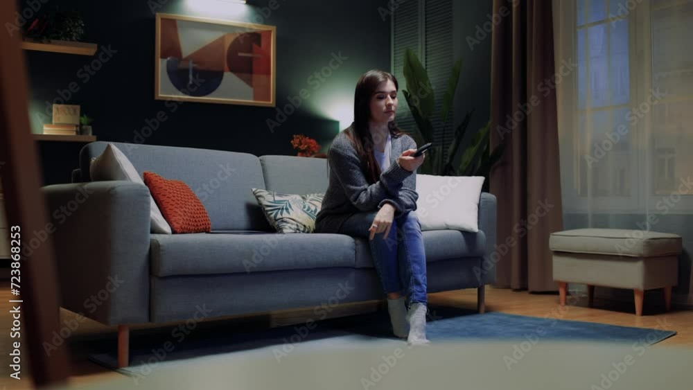 Pretty girl relaxing on couch, using remote control and choosing TV show or movies on television menu. Young woman sitting on sofa, holding TV remote while enjoying program, leisure time at home. Pretty girl relaxing on couch, using remote control and choosing TV show or movies on television menu. Young woman sitting on sofa, holding TV remote while enjoying program, leisure time at home.