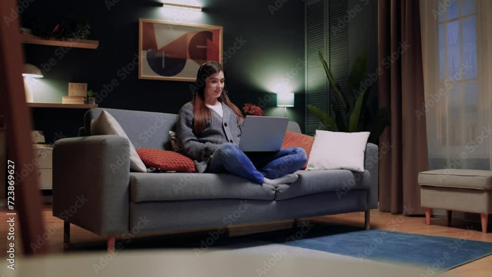 Portrait of cute beautiful smiling young lady video calling on laptop. Happy pretty woman student wearing wireless headphones looking at computer screen studying at home in evening remotely. Portrait of cute beautiful smiling young lady video calling on laptop. Happy pretty woman student wearing wireless headphones looking at computer screen studying at home in evening remotely.