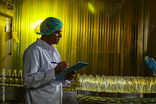 A factory worker inspects bottles on a beverage production line.