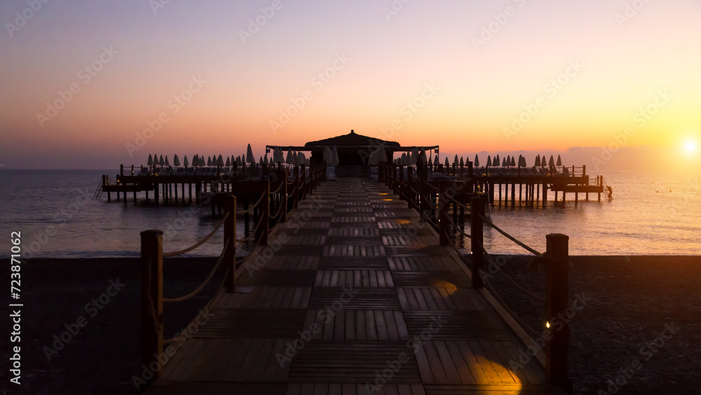 Early dark morning over the sea, the pier is barely lit by the first rays of the sun and electric lamps.