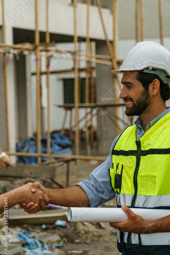 Foreman man with Yellow helmet holding plan roll shaking hand with someone in constuction site