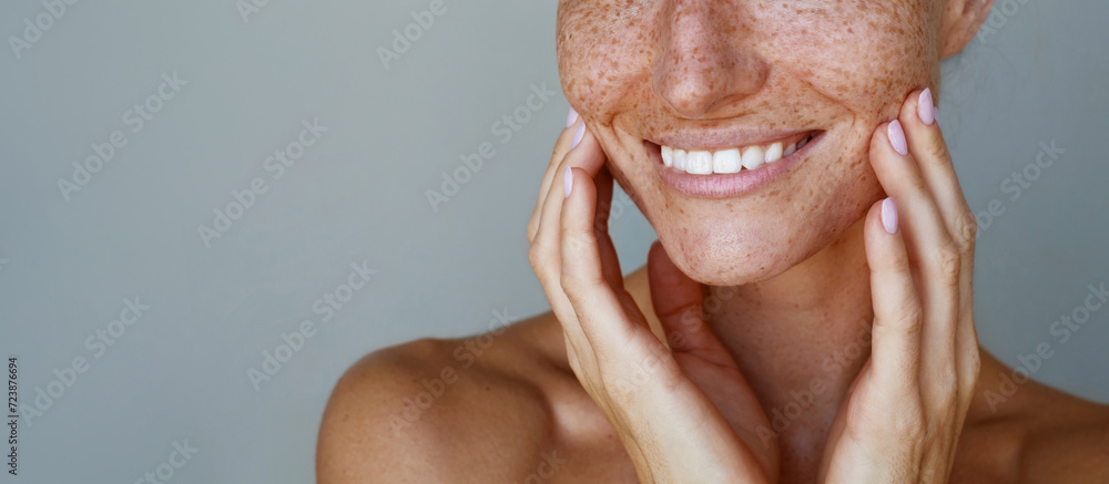 Naklejka premium Skin care. Freckles. Cropped portrait of a young woman is posing with a chin look against grey background. Natural beauty and glowing clean hydrated skin