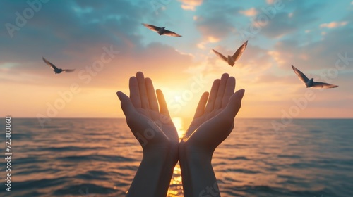 Hands open palm up worship with birds flying over calm water sunset background. Concept of praying for blessing from God. photo