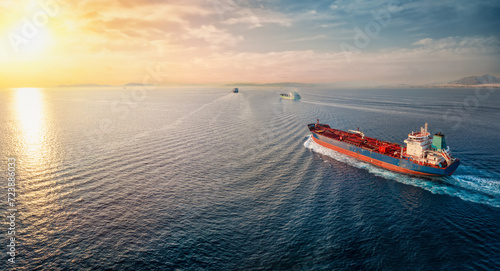 A group of cargo bulk ships and chemical goods or oil tanker sailing with speed over the ocean into the sunset photo