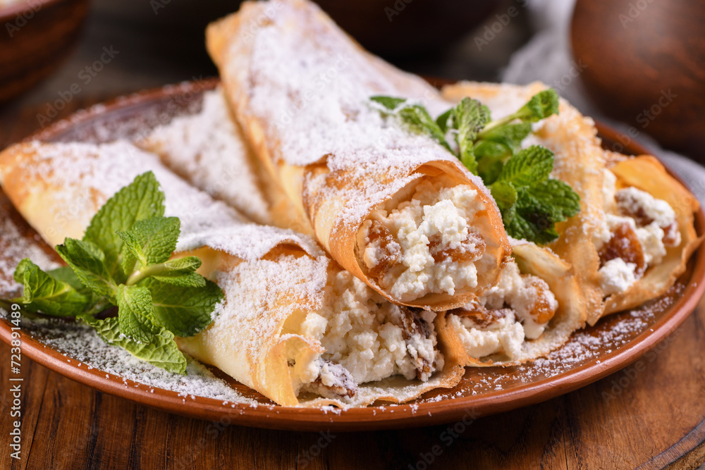 Thin pancakes filled with cottage cheese, honey and raisins, rolled in the form of a tube, sprinkled with powdered sugar, garnished with mint. Festive dish for the pagan Slavic holiday Maslenitsa