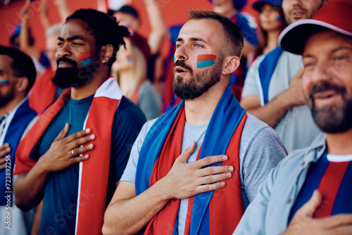 Obraz na plátne Group of sports fans with hand on heart singing national anthem during championship at stadium