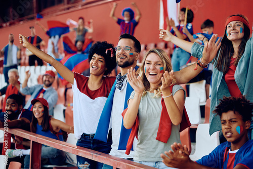 Group of happy friends cheering from stadium stands during sports match.