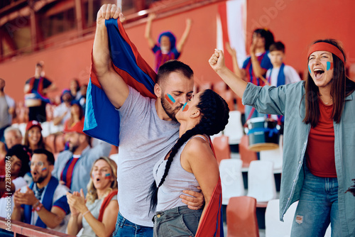 Fototapeta Naklejka Na Ścianę i Meble -  Couple of sports fans kissing while celebrating during match at stadium.