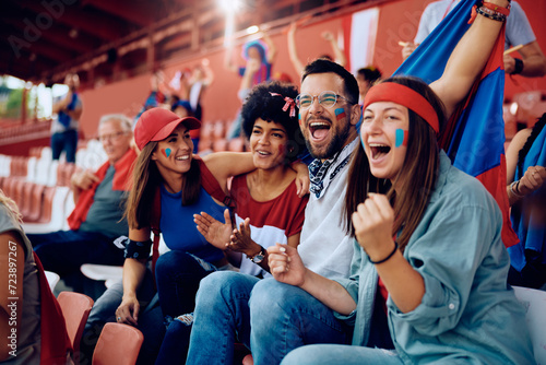 Multiracial group of happy friends cheering while watching sports game at stadium. photo