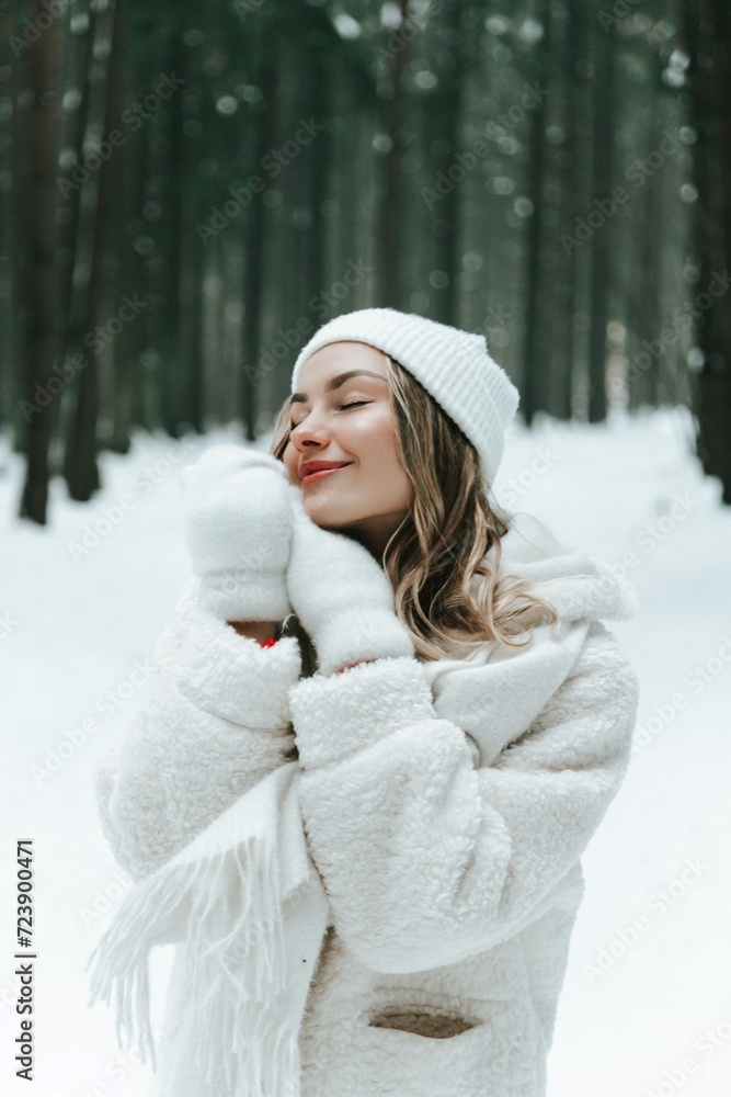 Young woman Enjoying snowy winter forest and warm clothes. Dressed white coat scarf hat and mittens fold palms to face Young woman Enjoying snowy winter forest and warm clothes. Dressed white coat scarf hat and mittens fold palms to face