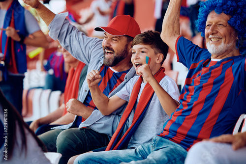 Happy boy cheering with his father and grandfather during sports match at stadium. photo