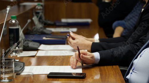 A man holds a pen with his fingers while sitting at a table during a conference or business meeting. Anonymous, unrecognisable, no face. Photo. Selective focus