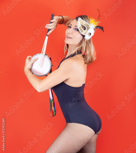 young woman, smiling with a Venetian mask, isolated on an orange background, playing a tambourine photo