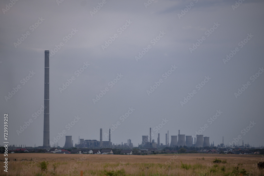 Oil refinery seen on the horizon on the wheat field at sunset. Polluting industry in the environment Oil refinery seen on the horizon on the wheat field at sunset. Polluting industry in the environment