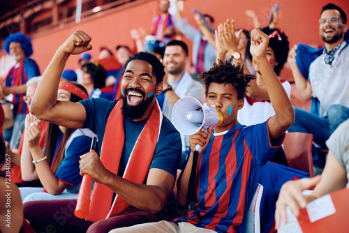 Cheerful black father and son cheering while watching sports match at stadium.