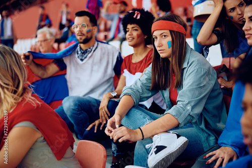 Displeased young woman and her friends watching sports match at stadium.