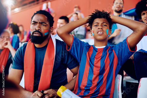 Black kid and his father displeased of their team losing match at stadium.