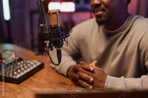 Cropped shot with focus on gold professional microphone on stand and Black man sitting at table recording live podcast