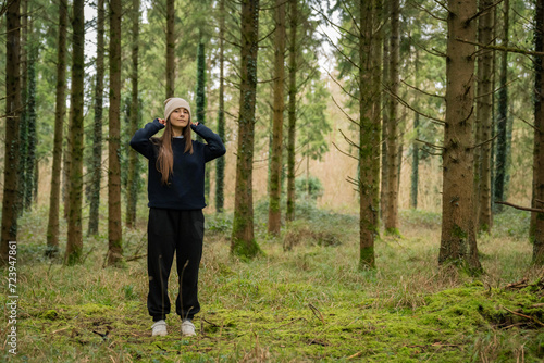 middle-aged white woman with brown hair, wearing a black sweater and a beige hat, in an Irish winter forest. © Araguatai