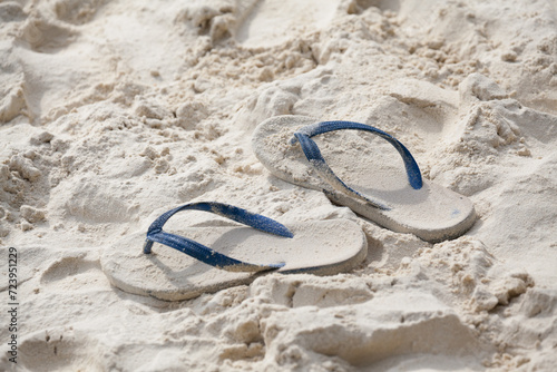 White pair of flip flops sticking up on a sandy beach with water