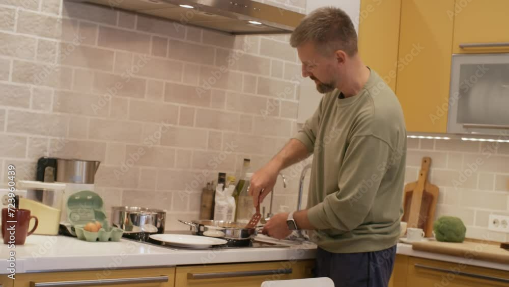 Handheld shot of bearded man scooping fried eggs with spatula and putting them on plate Handheld shot of bearded man scooping fried eggs with spatula and putting them on plate