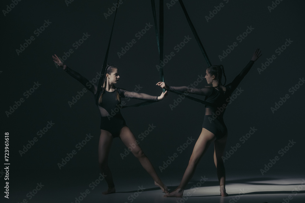 Portrait of two female acrobats in studio isolated on black background. Girls aerial dancers performing element with ropes. Portrait of two female acrobats in studio isolated on black background. Girls aerial dancers performing element with ropes.