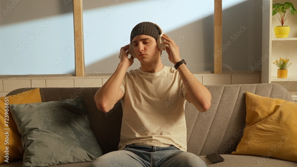 Fototapeta premium Portrait of young person in the room sitting on the couch. Man in headphones listening to music.