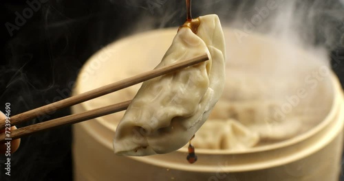 Super slow motion of organic soy sauce dripping on steamed homemade asian traditional recipe fresh pasta gyoza stuffed with meat kept with bamboo chopsticks in japanese chinese restaurant at 1000 fps. photo
