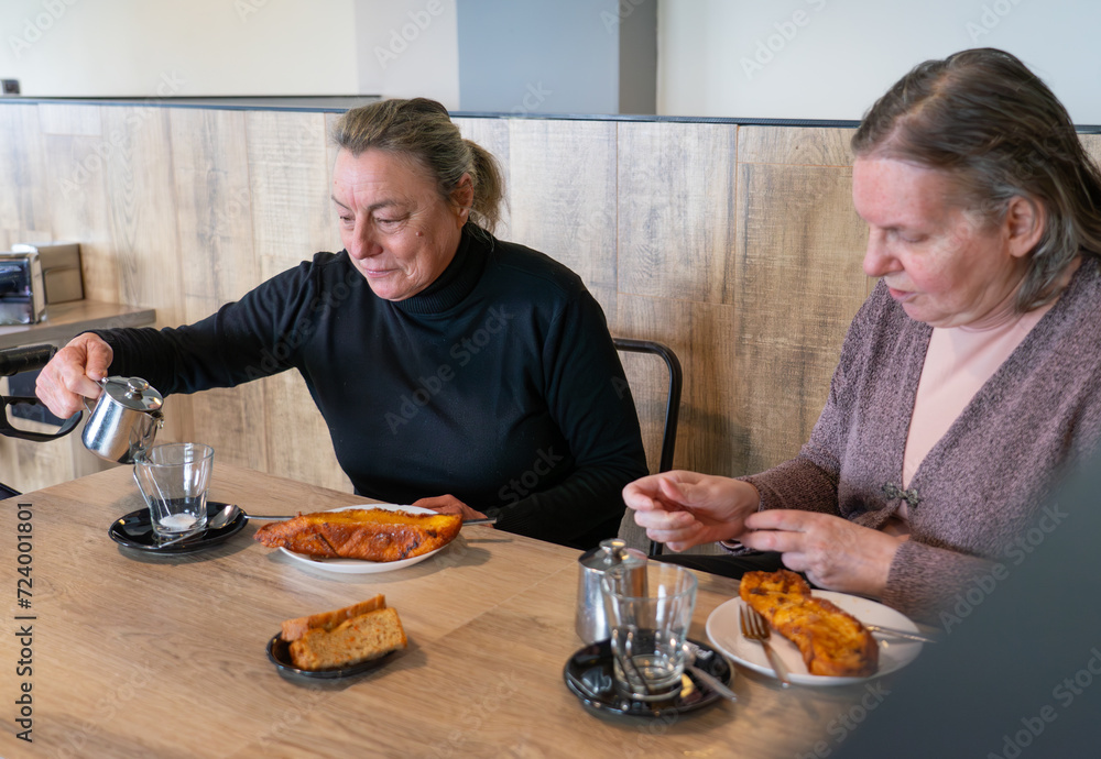 Two elderly friends in a cafeteria eating torrijas and tea Two elderly friends in a cafeteria eating torrijas and tea