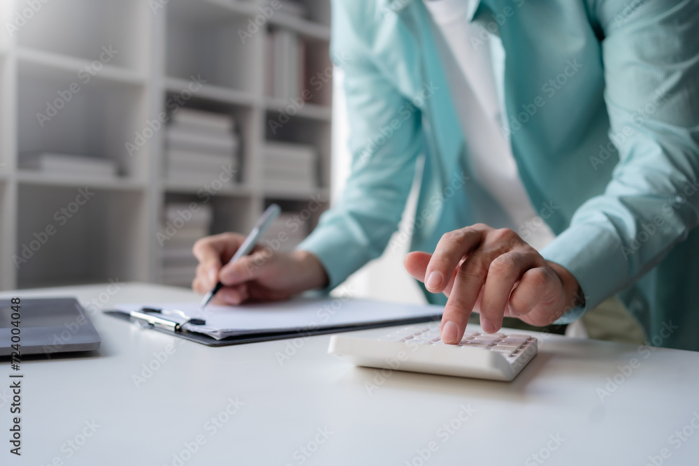 Business professional using a calculator and taking notes, financial planning or budgeting on a clipboard in an office. Business professional using a calculator and taking notes, financial planning or budgeting on a clipboard in an office.