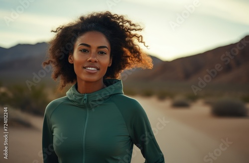 A woman stands alone in the center of a dry desert road surrounded by vast empty wilderness.