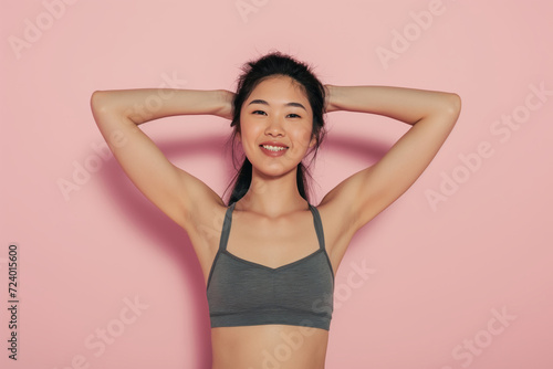 Asian woman in white t-shirt put her hands behind her head in against light pink studio background © Анастасия Бутко