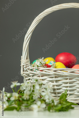 white wicker basket with colored eggs and spring flowers on the table, happy Easter concept