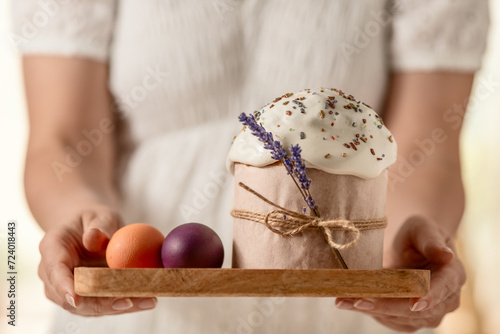 traditional Orthodox Easter cake and colored eggs, on a tray in women's hands, close-up on a light background. happy Easter