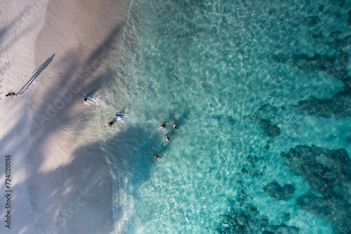 Aerial drone bird eye view in abstract mode of people swimming in a white sand beach with crystal clear waters in Bali Indonesia.