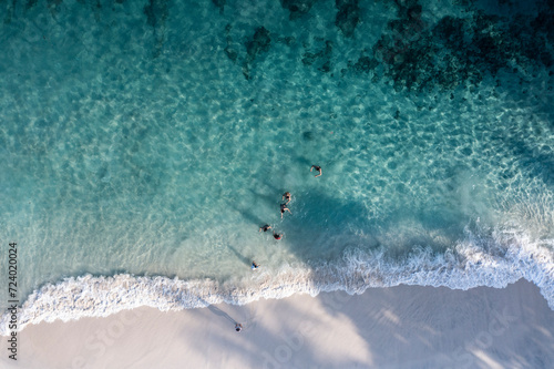Aerial drone bird eye view in abstract mode of people swimming in a white sand beach with crystal clear waters in Bali Indonesia.
