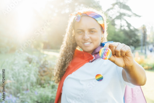 LGBTQ rainbow flag pin in the hand of young smiling lesbian activist. Round badge with Love is love message. Fight for equality, freedom and human rights. Celebrating Pride month. Selective focus. photo
