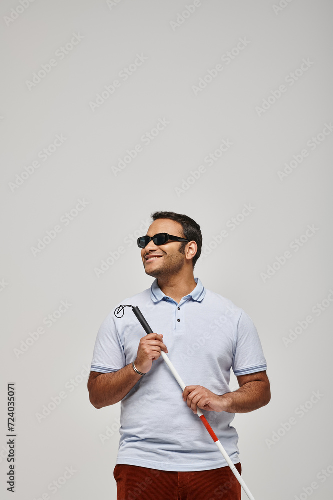 joyous indian blind man in blue tee shirt with glasses and walking stick posing on gray backdrop joyous indian blind man in blue tee shirt with glasses and walking stick posing on gray backdrop