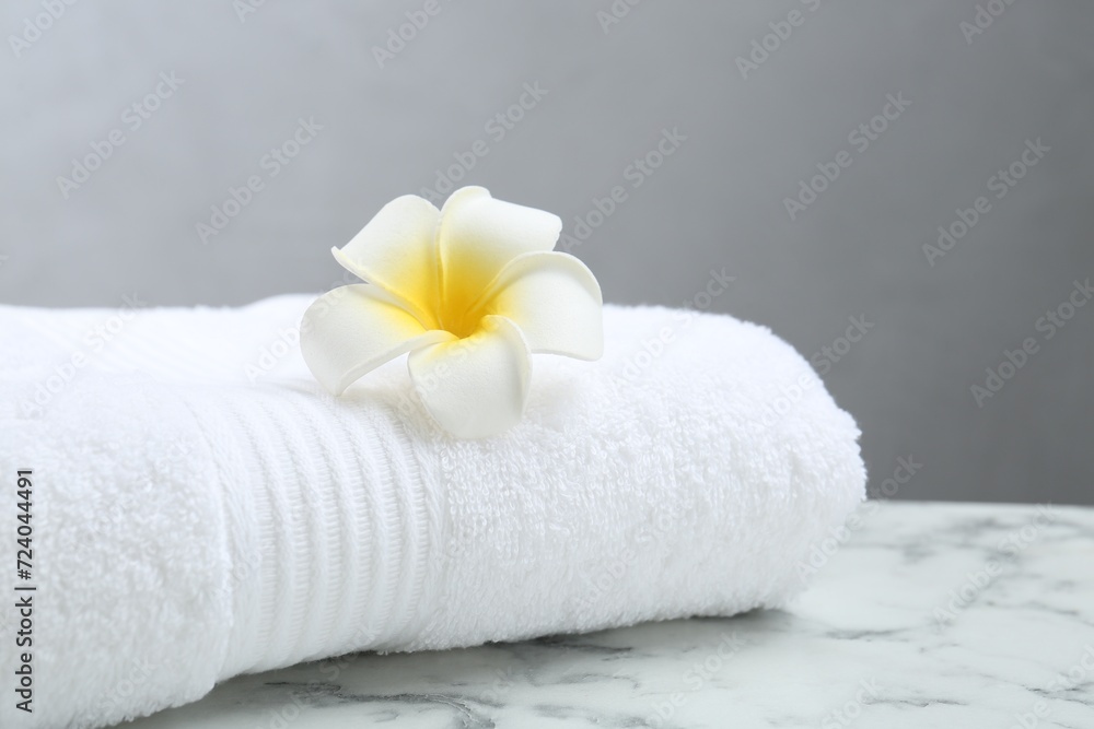 Folded terry towel and plumeria flower on white marble table, closeup. Space for text Folded terry towel and plumeria flower on white marble table, closeup. Space for text