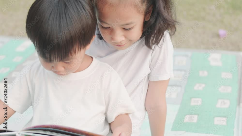 Close up faces and top view of two adorable asian kids, brother and sister, who are reading book together in the park with beautiful sunlight during summer shows concept of family learning of child. Close up faces and top view of two adorable asian kids, brother and sister, who are reading book together in the park with beautiful sunlight during summer shows concept of family learning of child.