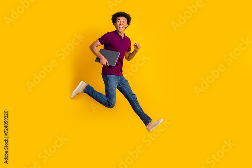 Full length photo of crazy funky man wear trendy purple polo carrying netbook hurrying store isolated on yellow color background