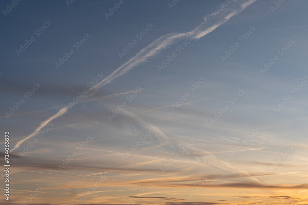 Paris, France - 01 28 2024: Sky Background. Detail view of a blue sky with colored clouds and aircraft trail at sunrise.