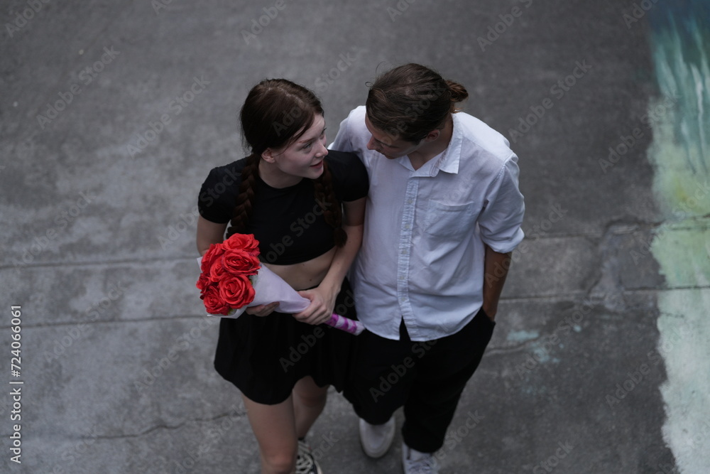 top aerial view of couple young man and woman walking and holding the red bouquet rose flowers at outdoor street. Concept couple life with love and happy moment.