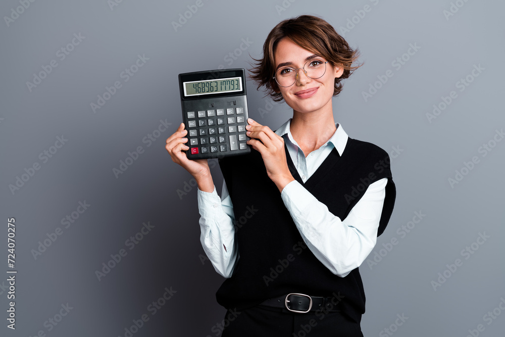 Portrait of intelligent positive girl with bob hairdo dressed waistcoat in eyewear showing calculator isolated on gray color background Portrait of intelligent positive girl with bob hairdo dressed waistcoat in eyewear showing calculator isolated on gray color background