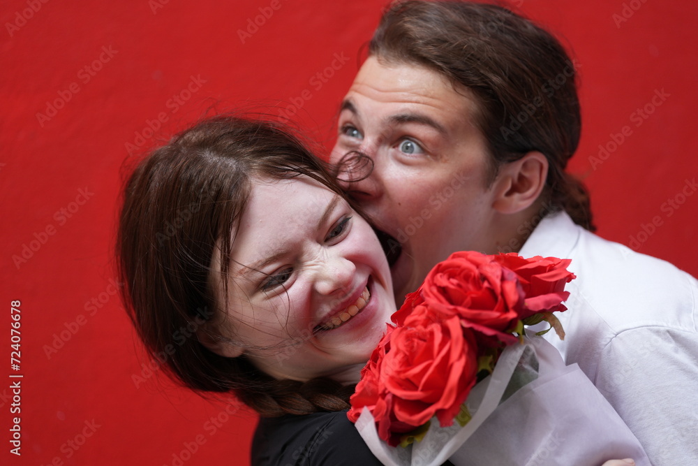 couple young man and woman hugging and holding the red bouquet rose flowers at red wall background. Concept couple life with love and happy moment. couple young man and woman hugging and holding the red bouquet rose flowers at red wall background. Concept couple life with love and happy moment.