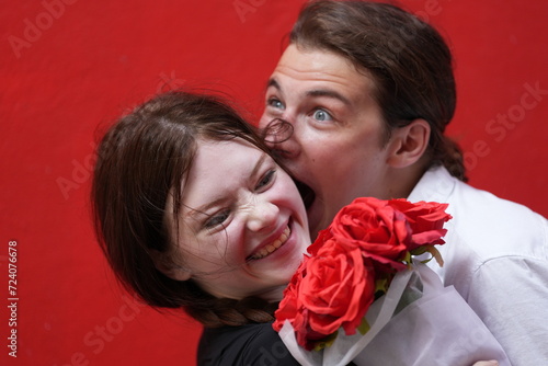 couple young man and woman hugging and holding the red bouquet rose flowers at red wall background. Concept couple life with love and happy moment.