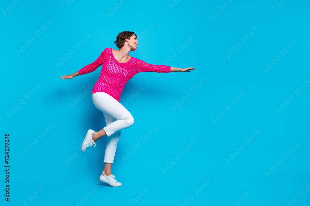 Full length photo of positive sweet woman wear knitted neon shirt hands arms sides flying empty space isolated blue color background