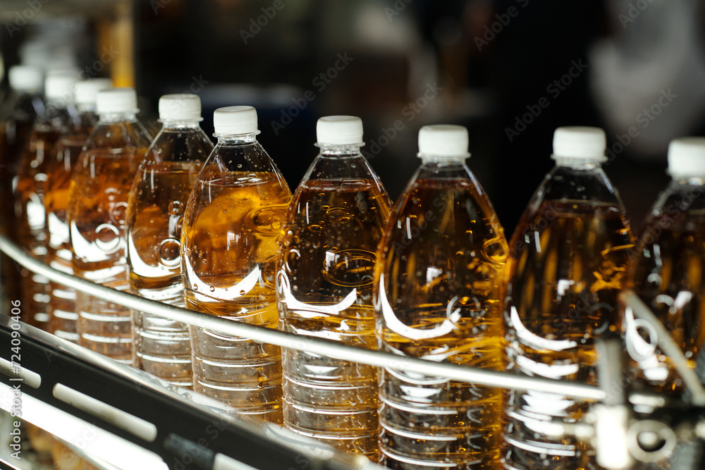 Row of transparent plastic bottles with soda or lemonade packed with white caps moving along assembly line or belt conveyor