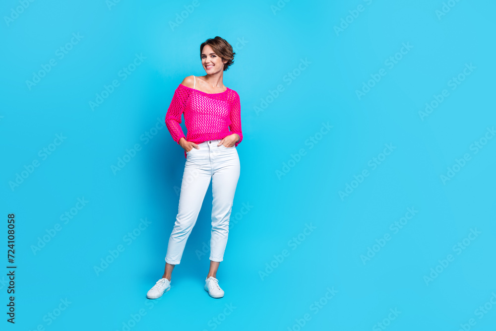 Full length photo of positive cute girl wear neon knitted shirt hands pockets empty space isolated blue color background Full length photo of positive cute girl wear neon knitted shirt hands pockets empty space isolated blue color background